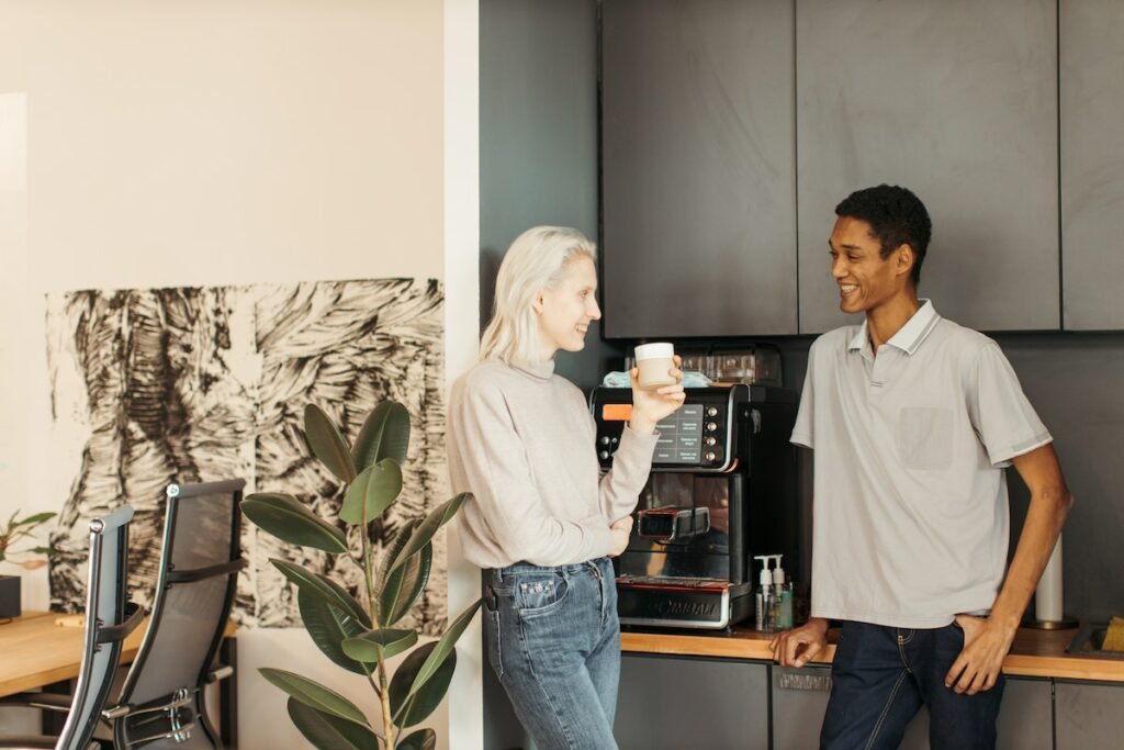 Two people standing next to a Coffee Man Beverage Services coffee machine in an office.