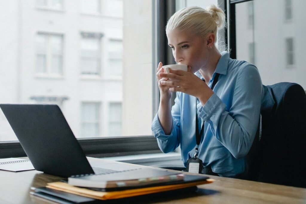 A woman sitting at a desk with a laptop and a cup of coffee from Coffee Man Beverage Services.