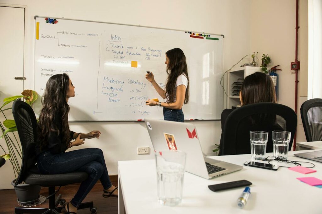 A group of women in a meeting room with a whiteboard, discussing strategies for water service filtration and examining different paper products for their coffee break supplies. - Coffee Man A group of women in a meeting room with a whiteboard, discussing strategies for water service filtration and examining different paper products for their coffee break supplies.
