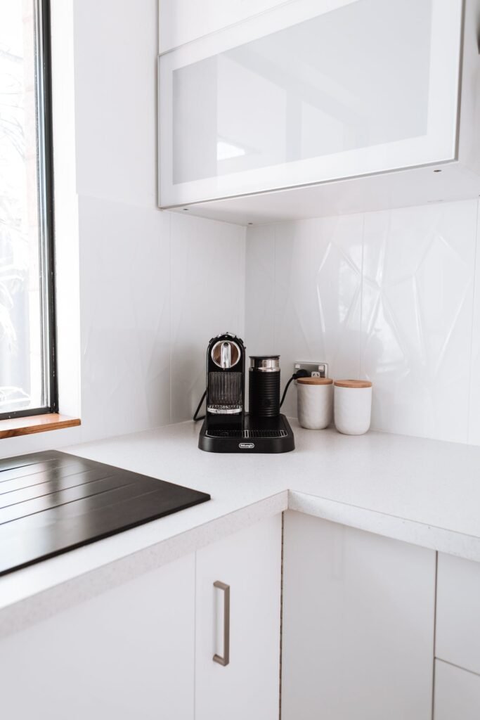 A white kitchen with a coffee maker and a window, perfect for corporate office refreshment.